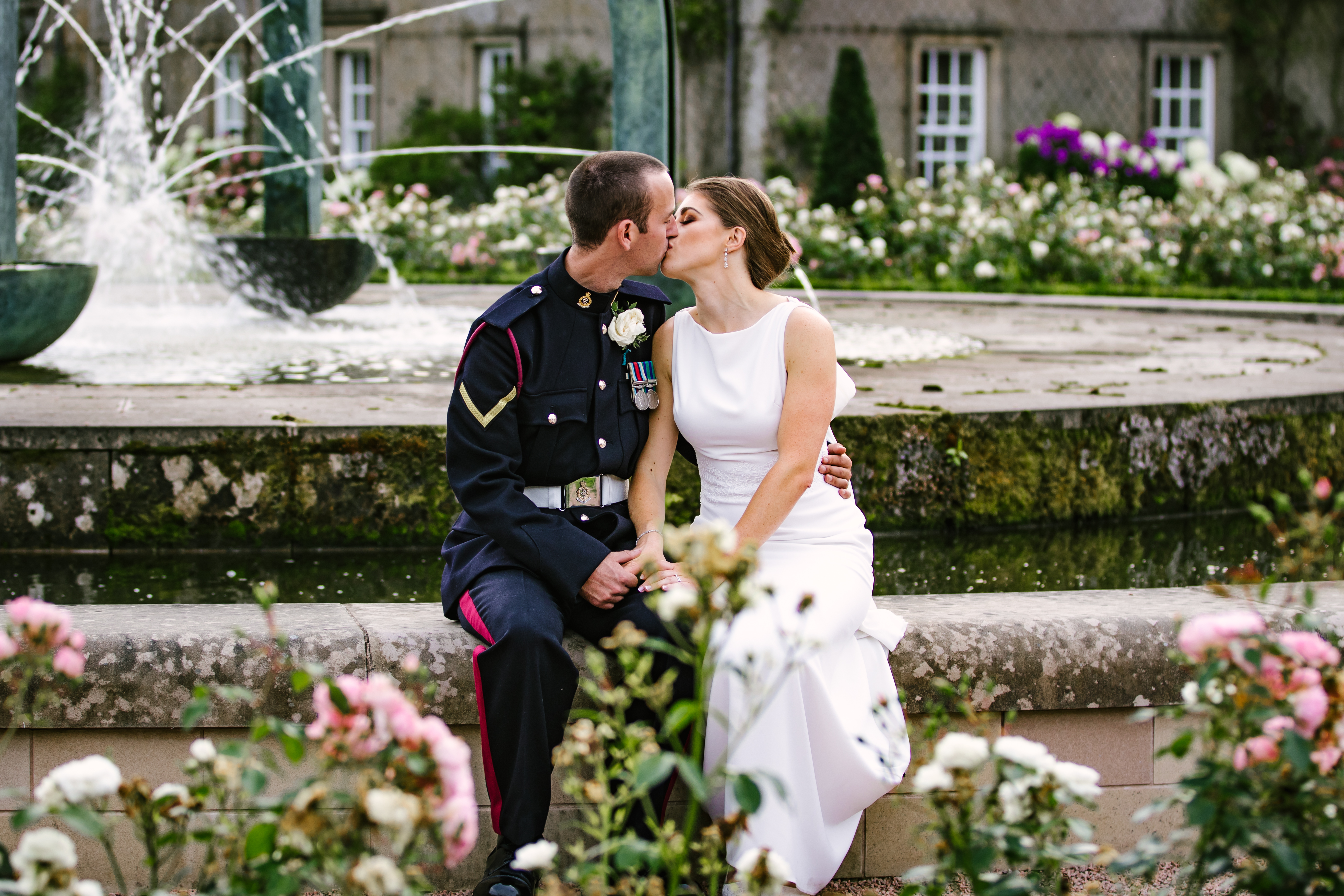 Anna & David — military groom and bride sharing a kiss beside a fountain in the rose garden